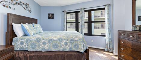 A bedroom with a bed, wooden dresser, and a window with curtains.