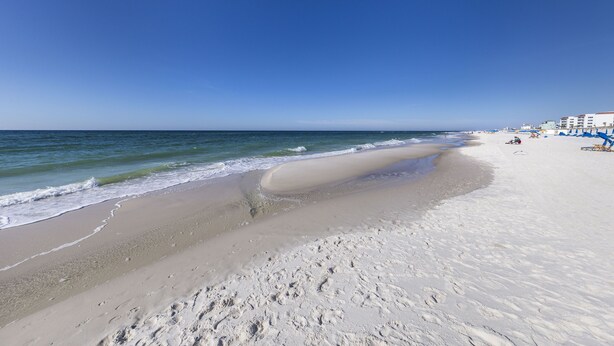 A beach with a clear sky, sandy shore, and buildings in the background. - Harbour Place 206 (Orange Beach)