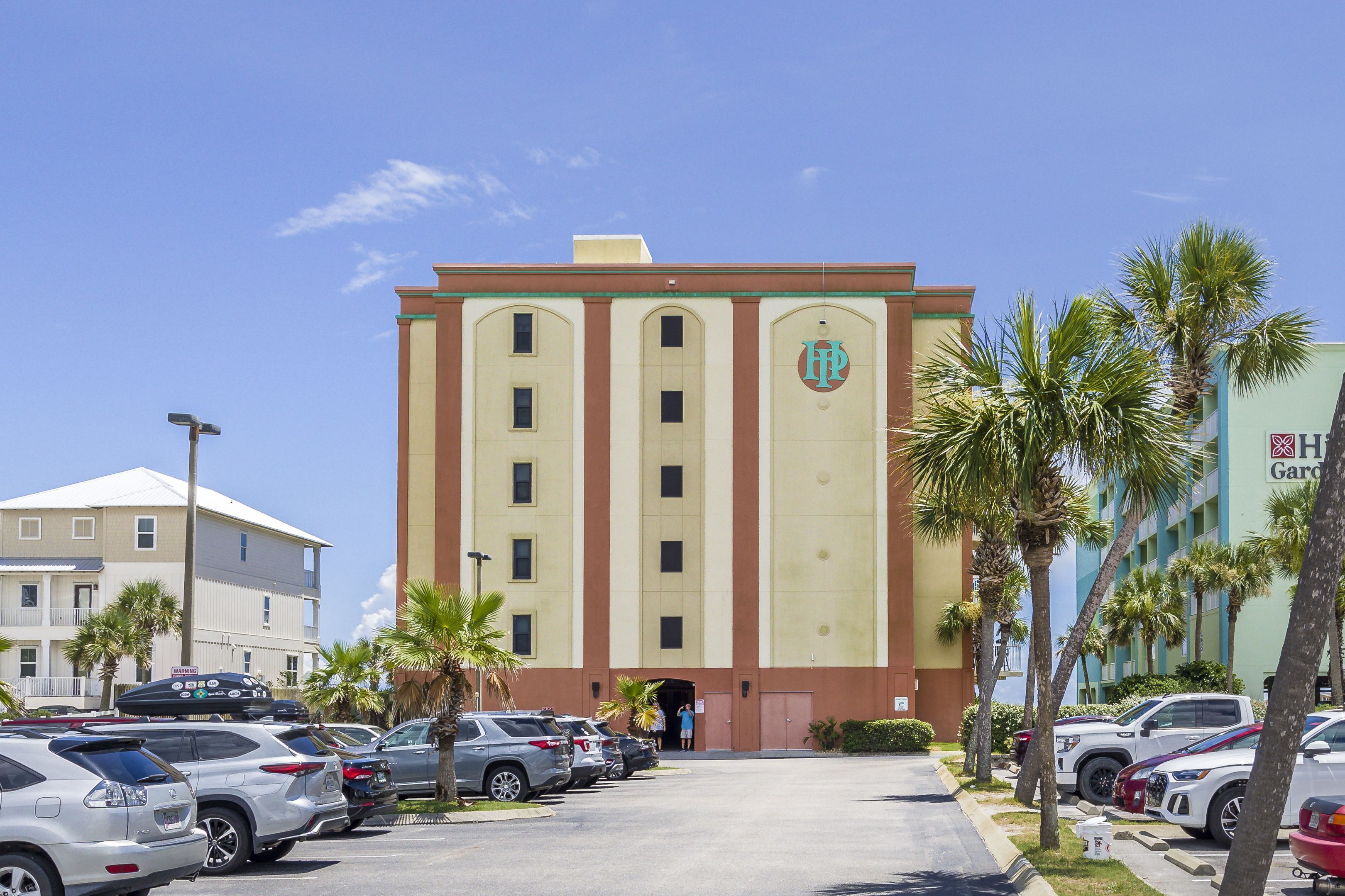 A hotel with a central entrance, parking lot, and palm trees.