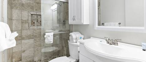 A bathroom with a glass-enclosed shower, a white toilet, a sink with a mirror above it, and a cabinet with a towel rack.