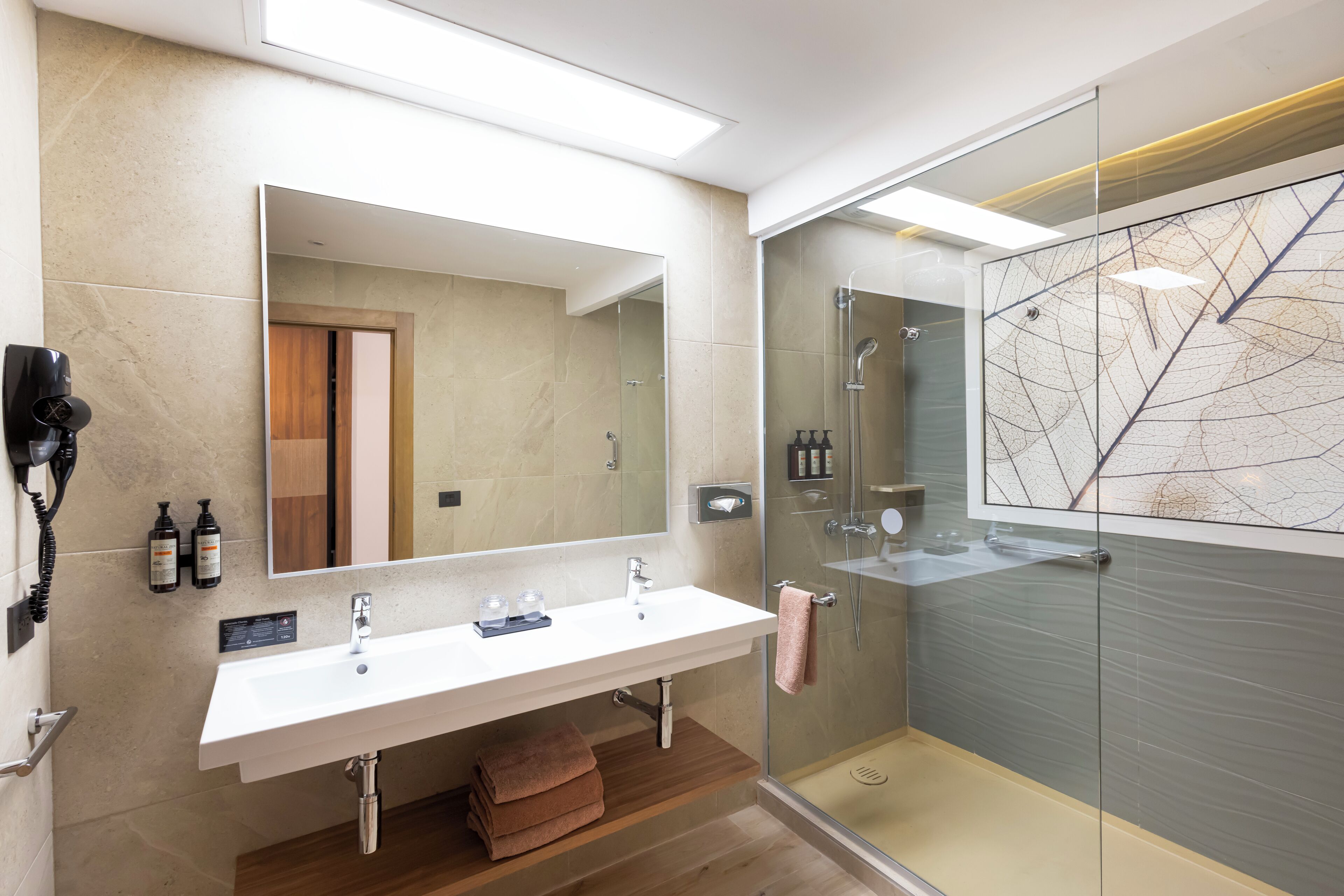A modern bathroom with a large mirror, a white sink, a glass shower enclosure, and a wooden vanity.