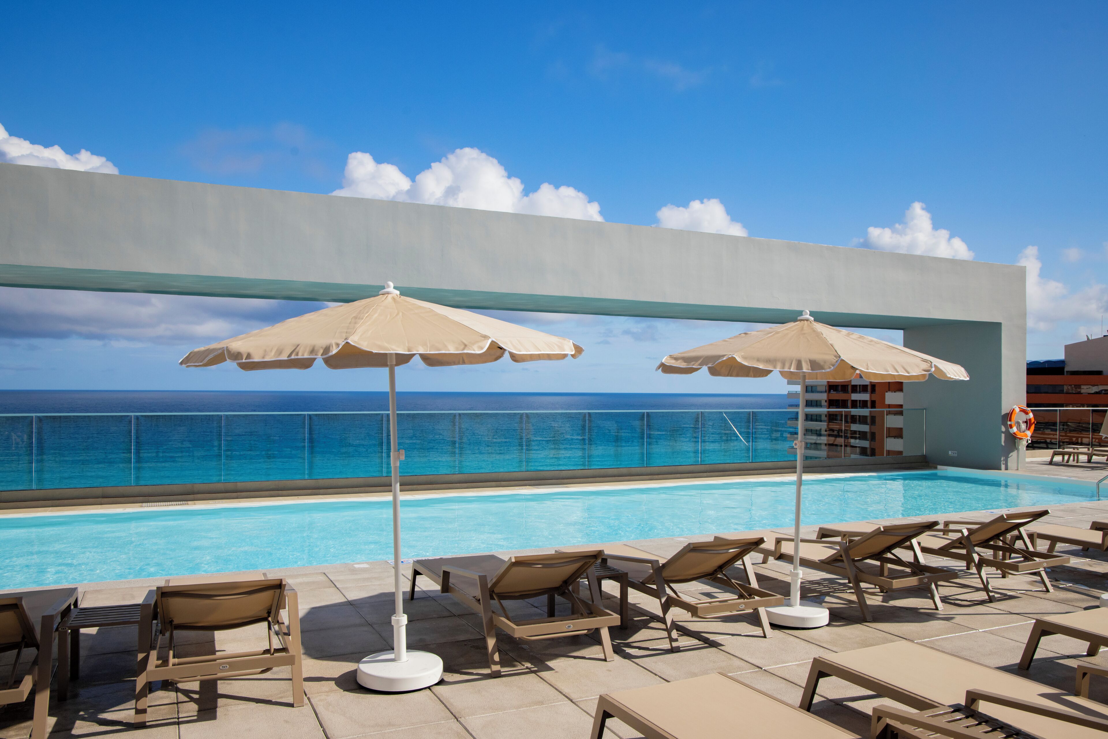 Ein Poolbereich mit Liegest ühlen und Sonnenschirmen mit Blick auf das klare, blaue Meer.