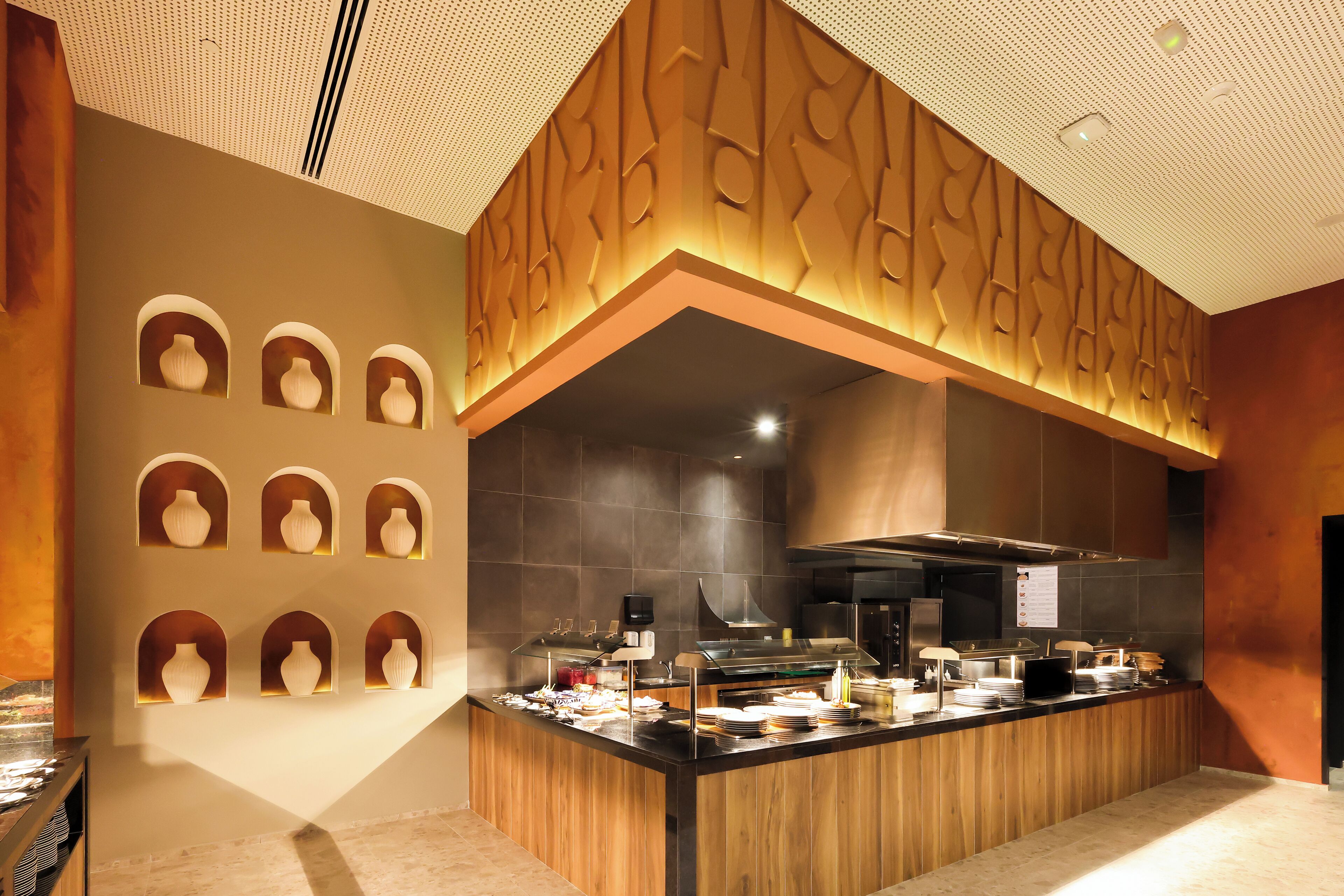 Una cocina moderna con una isla central, hornos integrados y una pared decorativa con iluminación empotrada.
