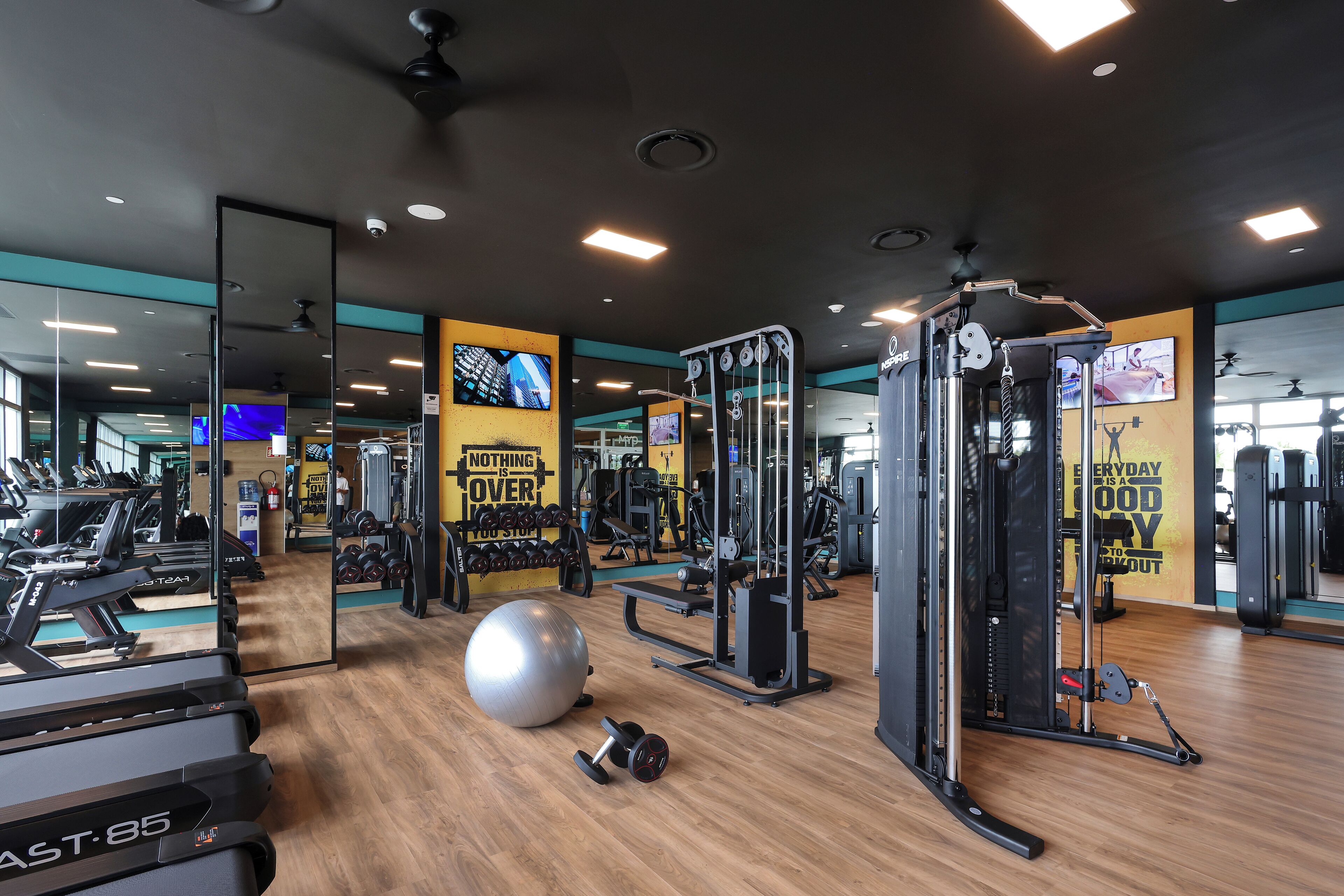 Un gimnasio con cintas de correr, una pelota de ejercicios grande y máquinas de pesas.