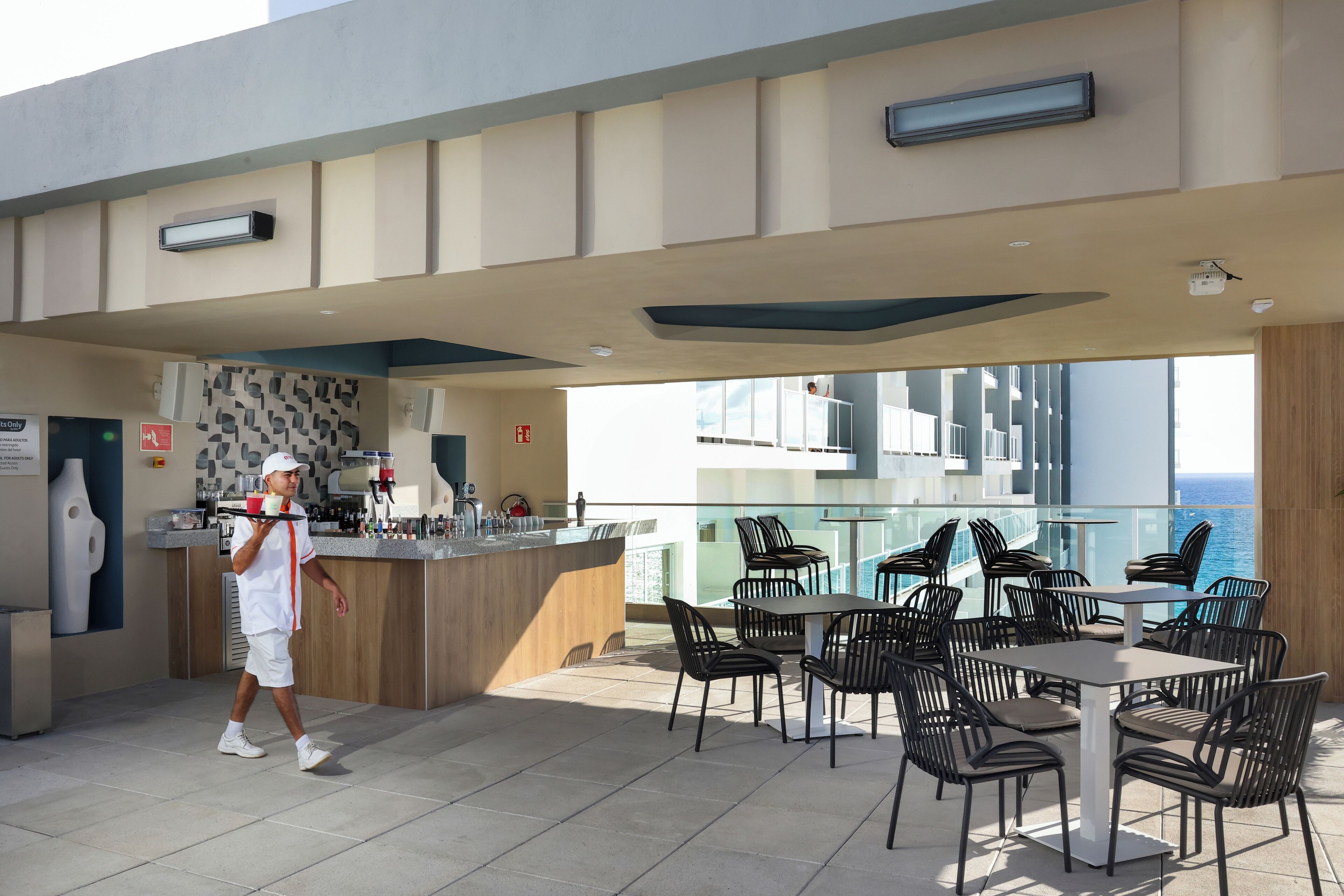 Zona pranzo all'aperto moderna con un bancone bar, sedie nere e vista sull'oceano.