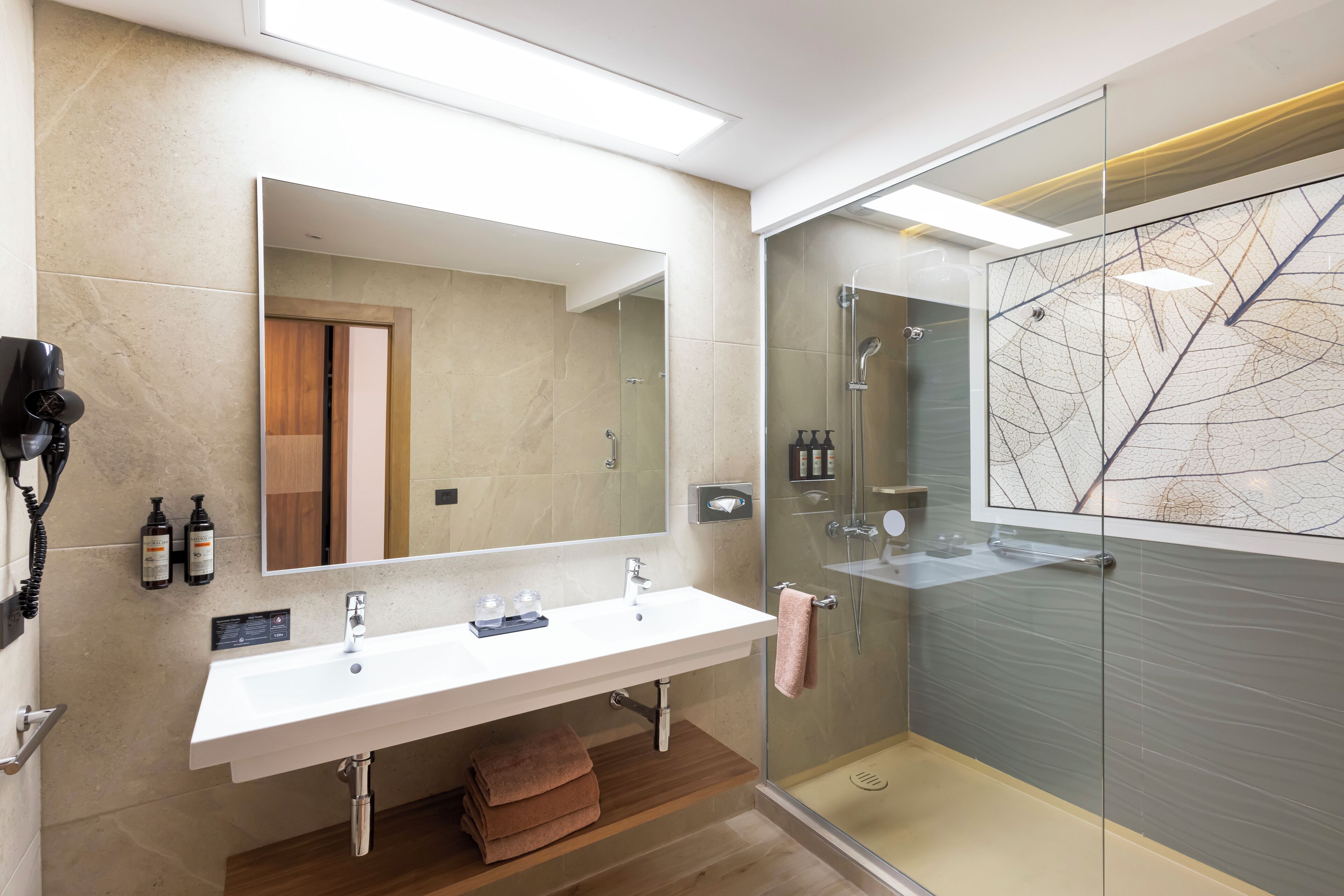 A modern bathroom with a large mirror, a double sink, and a glass-enclosed shower.
