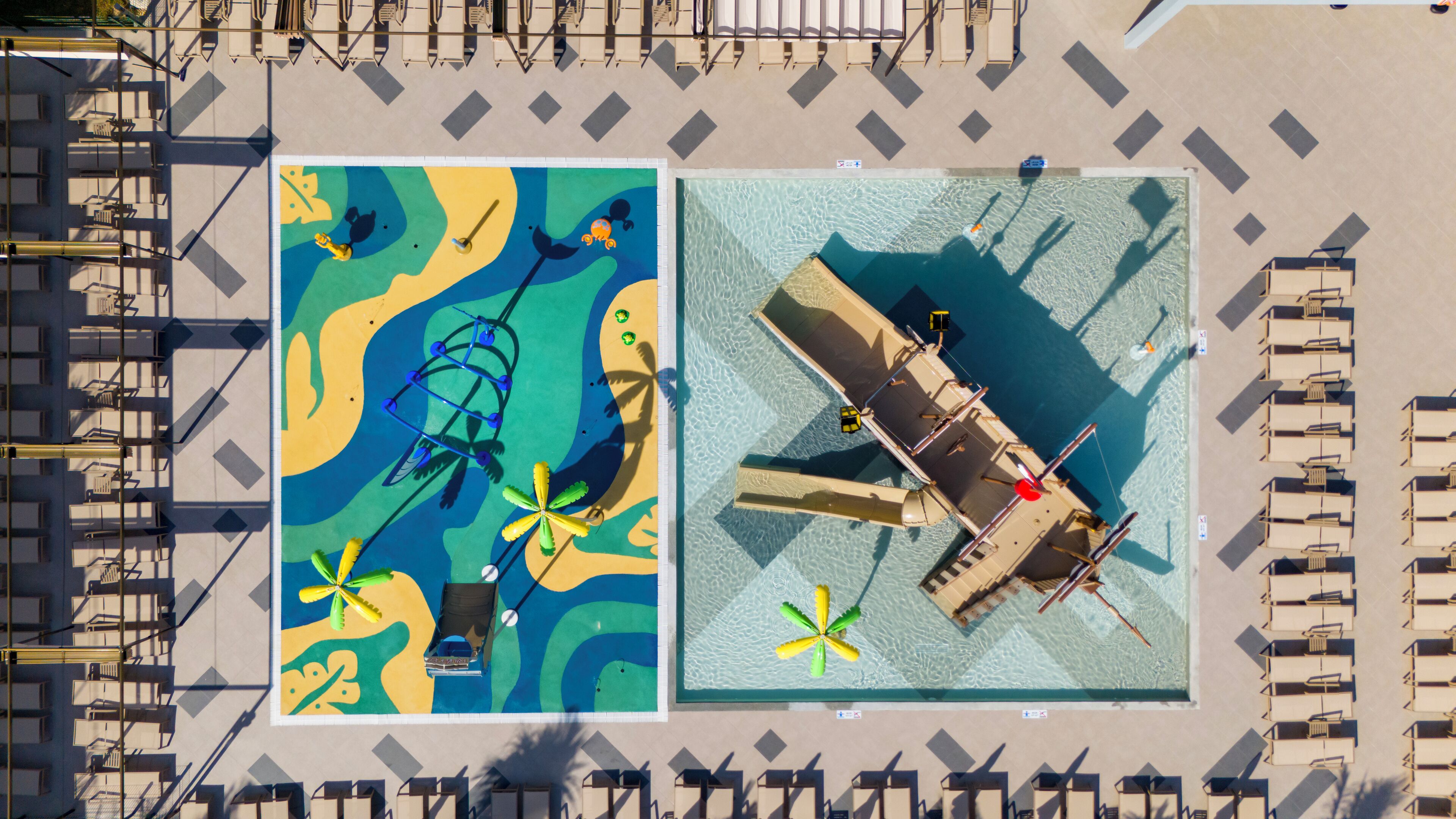 An aerial view of a hotel with a pool area, sun loungers, and a lifeguard stand.