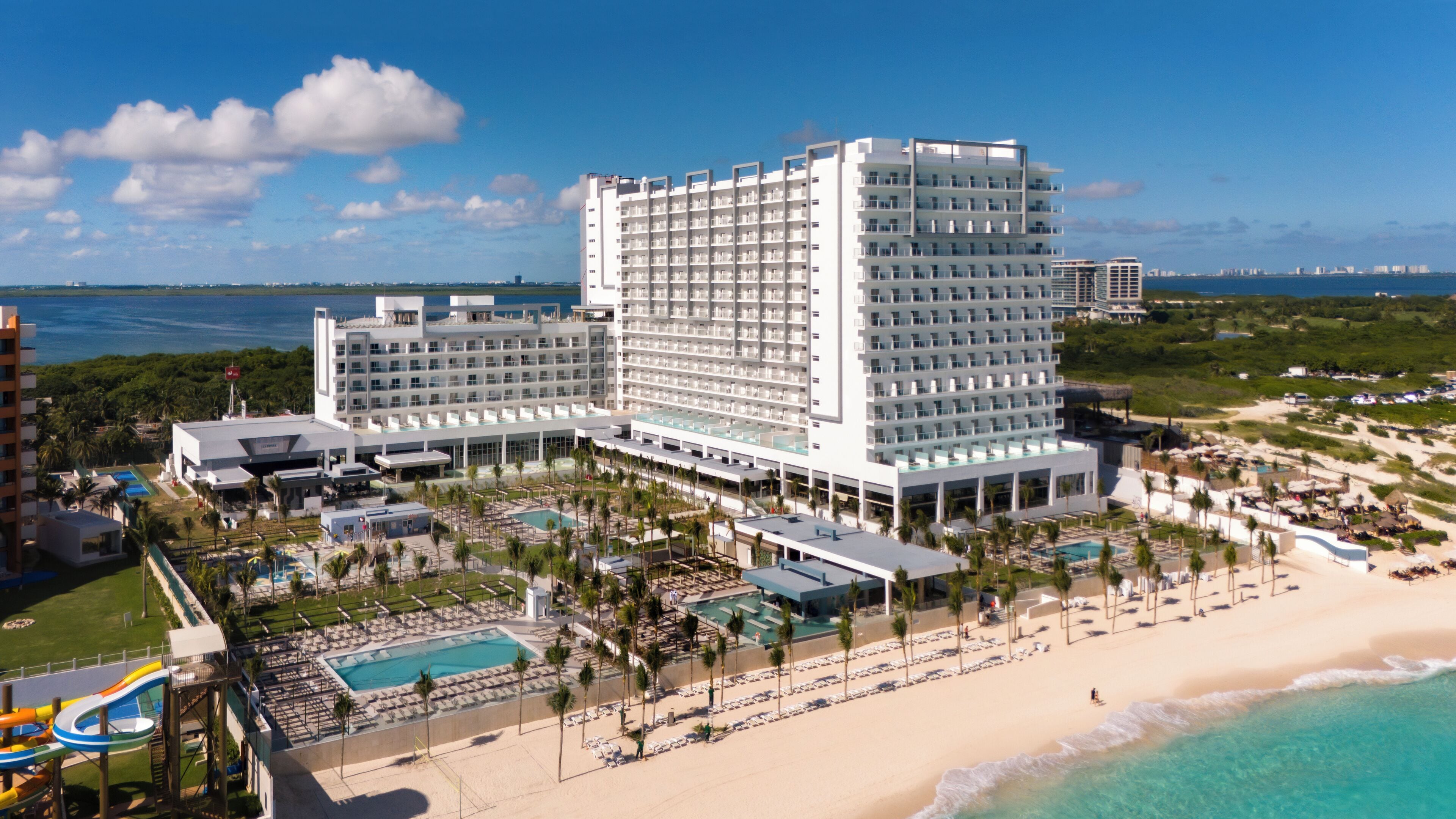 A large resort hotel with multiple buildings, a pool area, and a beach.