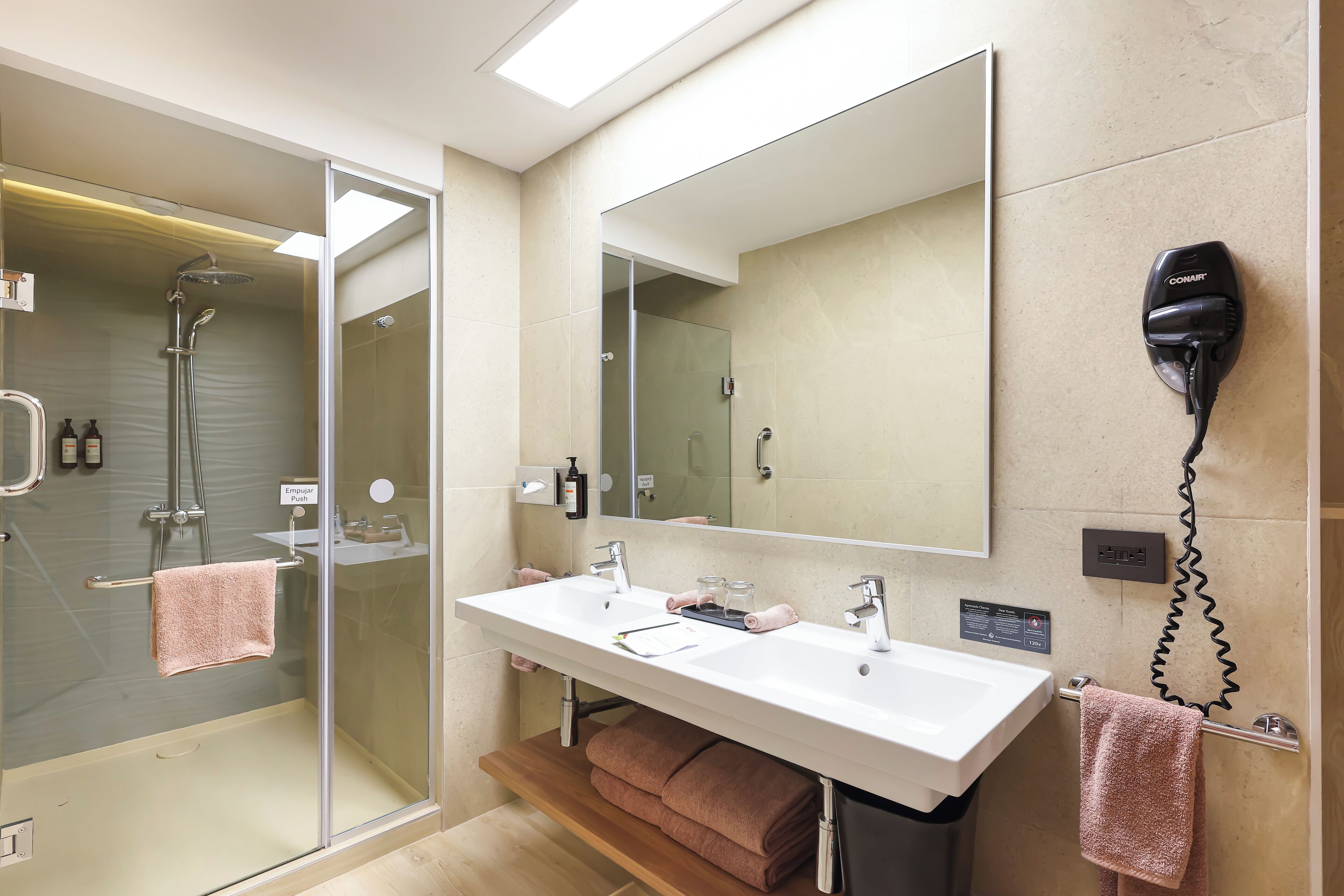 A modern bathroom with a large mirror, a shower, and a hairdryer mounted on the wall.