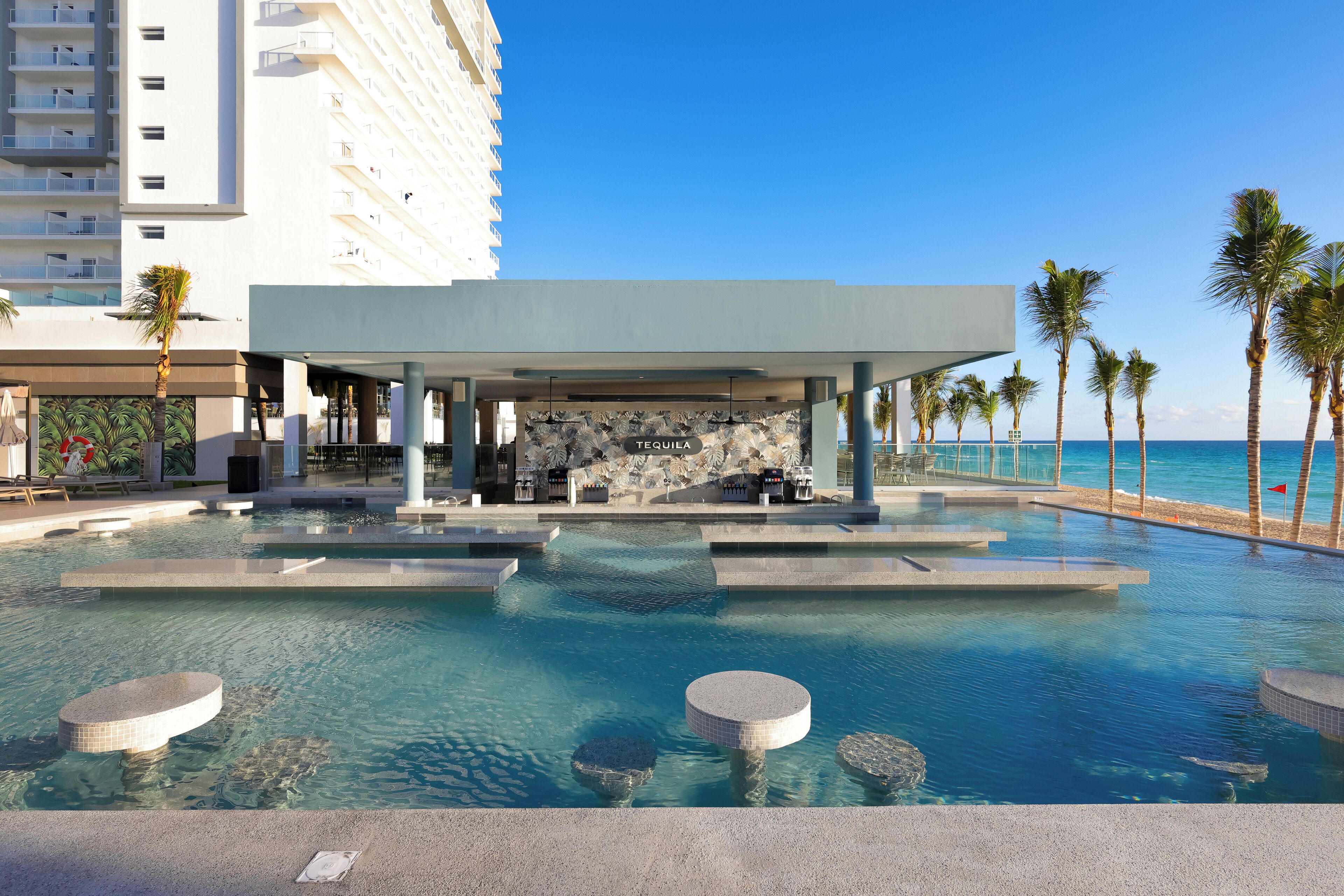A pool area with a bar, palm trees, and a view of the ocean.