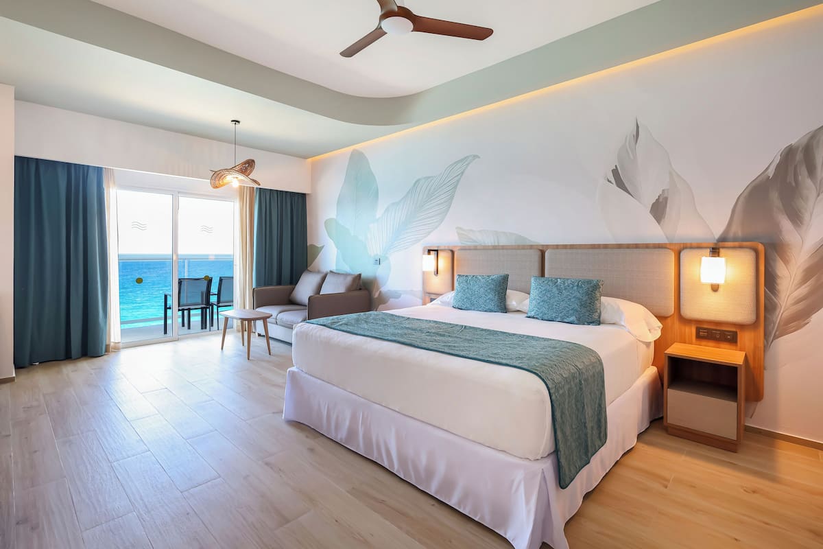 Una habitación de hotel con una cama grande, un escritorio y vista al océano.