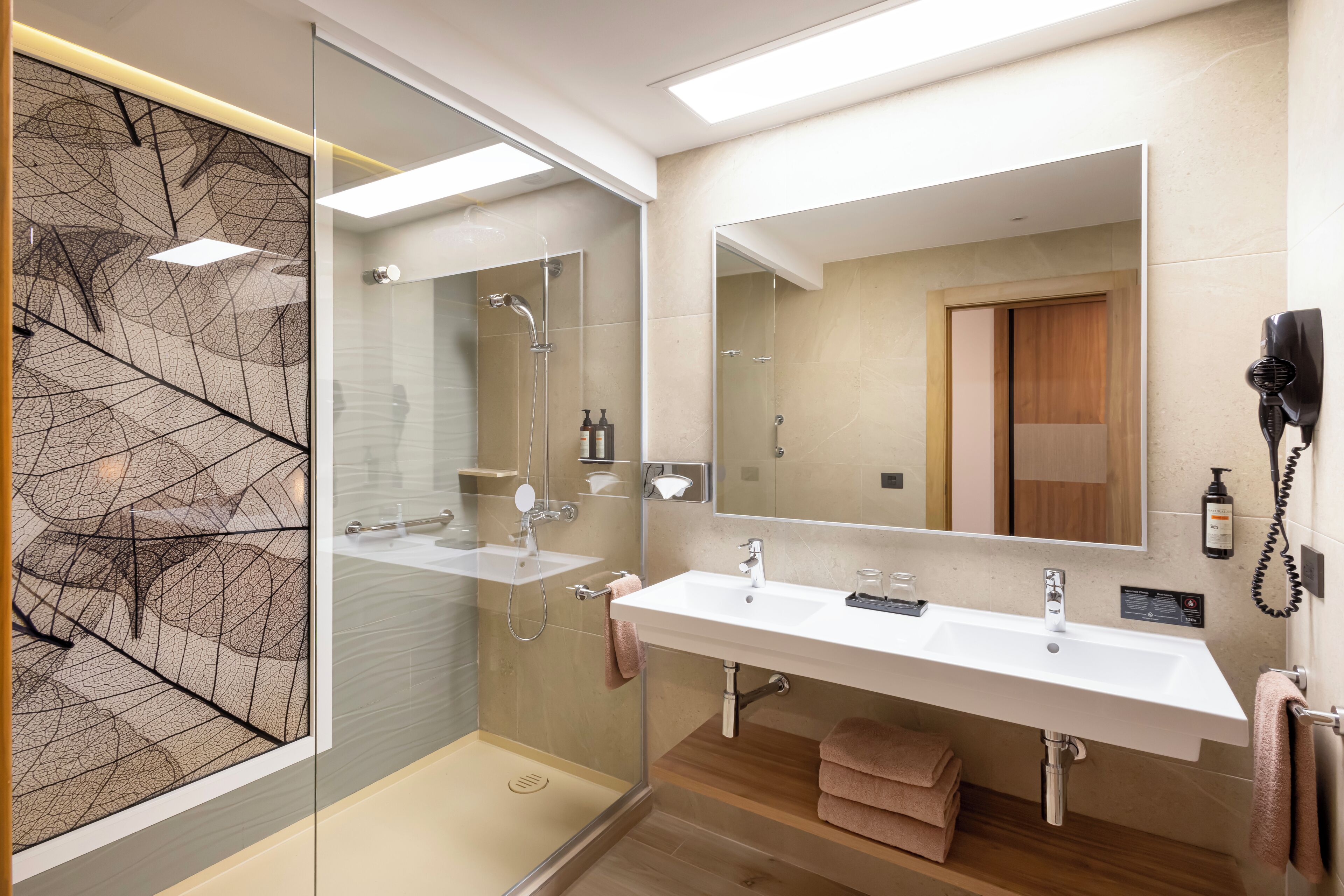 A modern bathroom with a glass shower enclosure, two sinks, and a large mirror.
