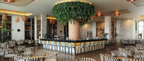 A spacious lobby with a central bar area, multiple seating arrangements, and a large hanging plant.