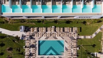 Vista aérea de un hotel con múltiples piscinas, tumbonas y una piscina central con un diseño geométrico distintivo.