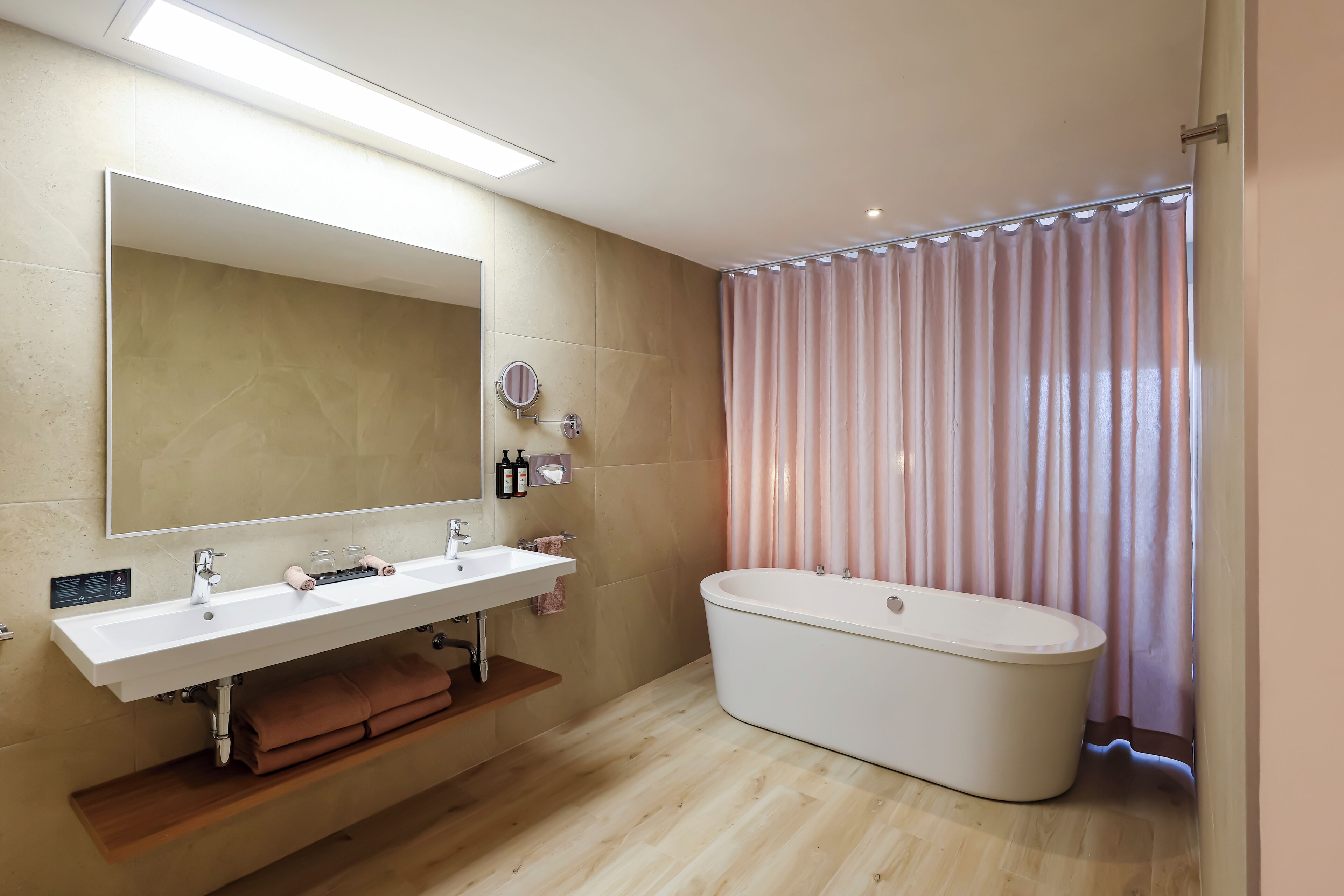 A modern bathroom with a large mirror, a white sink, a bathtub, and a vanity with a towel rack.