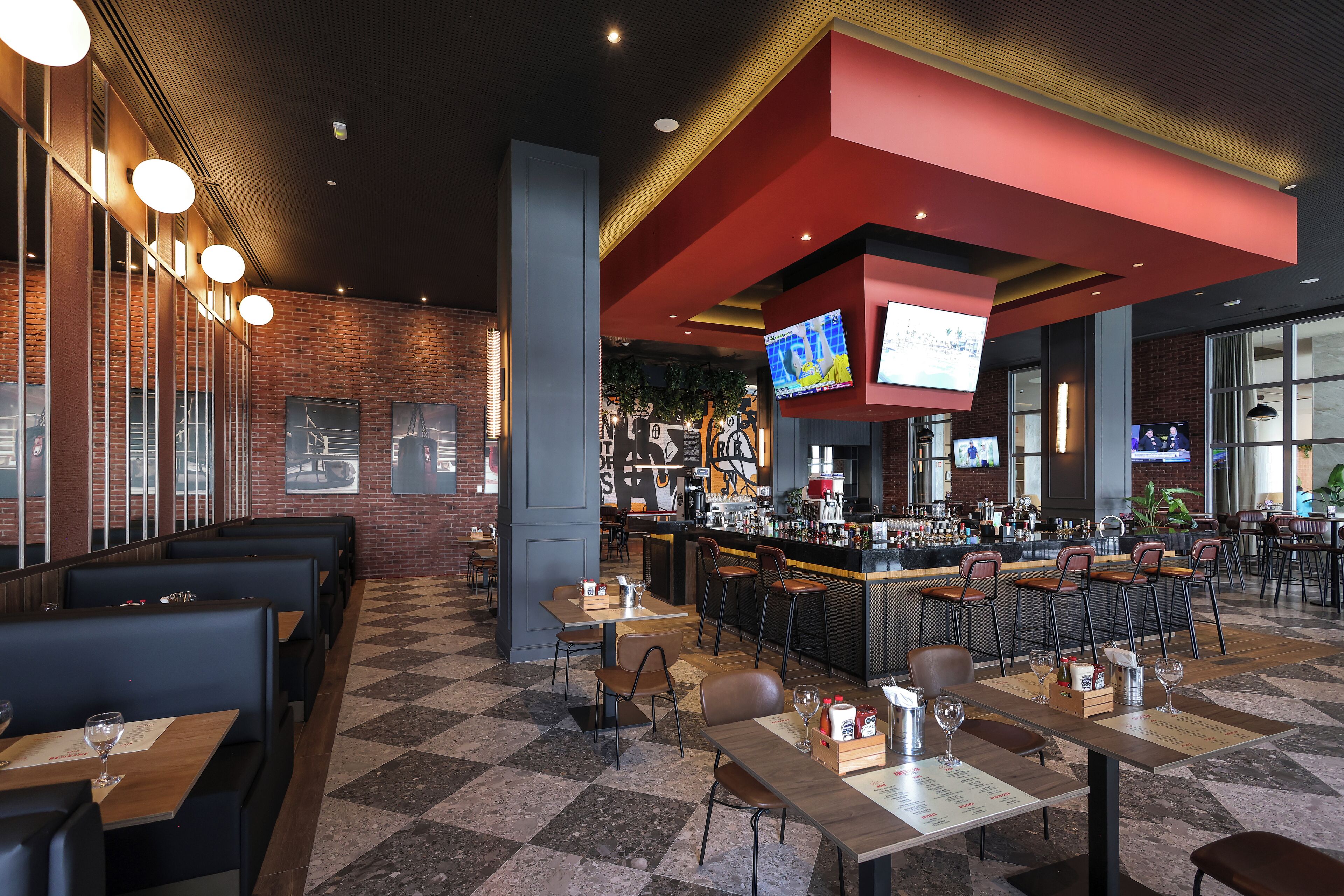 Un restaurante moderno con cabinas y mesas, una zona de bar y varias televisiones.