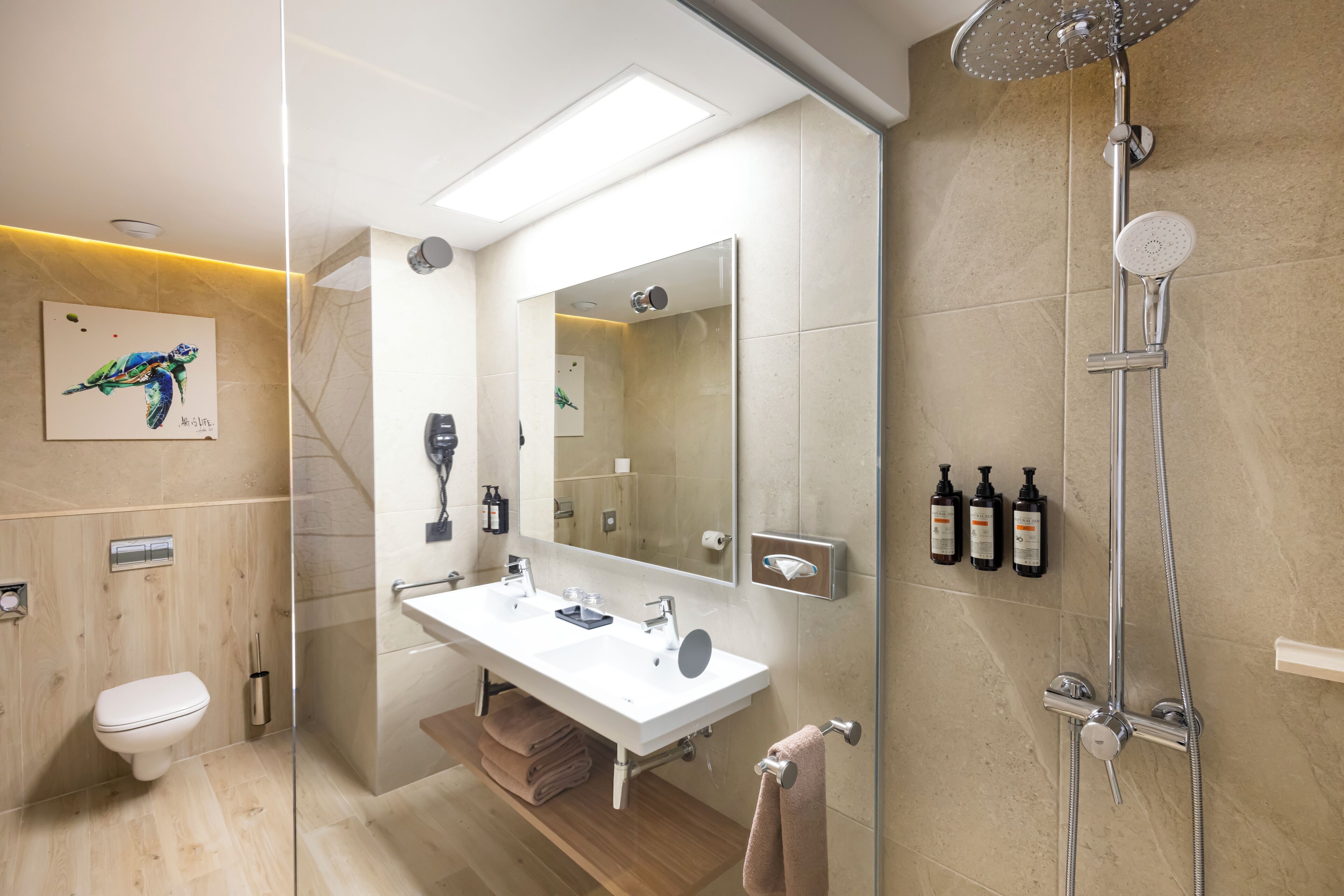Un baño moderno con ducha de vidrio, un espejo grande y un lavamanos blanco.