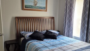 Un dormitorio con cama, ventilador de techo, un cuadro de un barco en la pared y una ventana con cortinas.