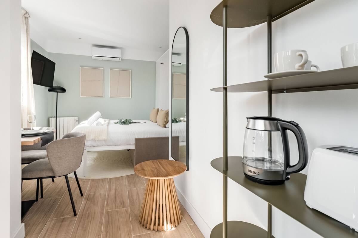 Habitación de hotel moderna con una cama, un escritorio con una silla, una cafetera y un estante con tazas.