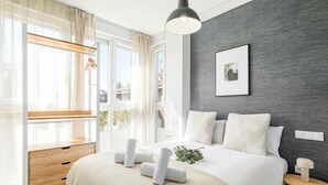 Ein modernes Schlafzimmer mit einem großen Bett, Nachttischen, einem Fenster mit Vorhängen und einer Wand mit Grau-Struktur.