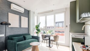 Ein modernes Wohnzimmer mit einem grünen Sofa, einem runden Holztisch und einem Essbereich mit Tisch und Stühlen.
