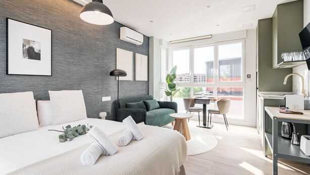 Ein modernes Hotelzimmer mit einem großen Bett, einem Schreibtisch und einem Balkon mit Blick auf die Stadt.