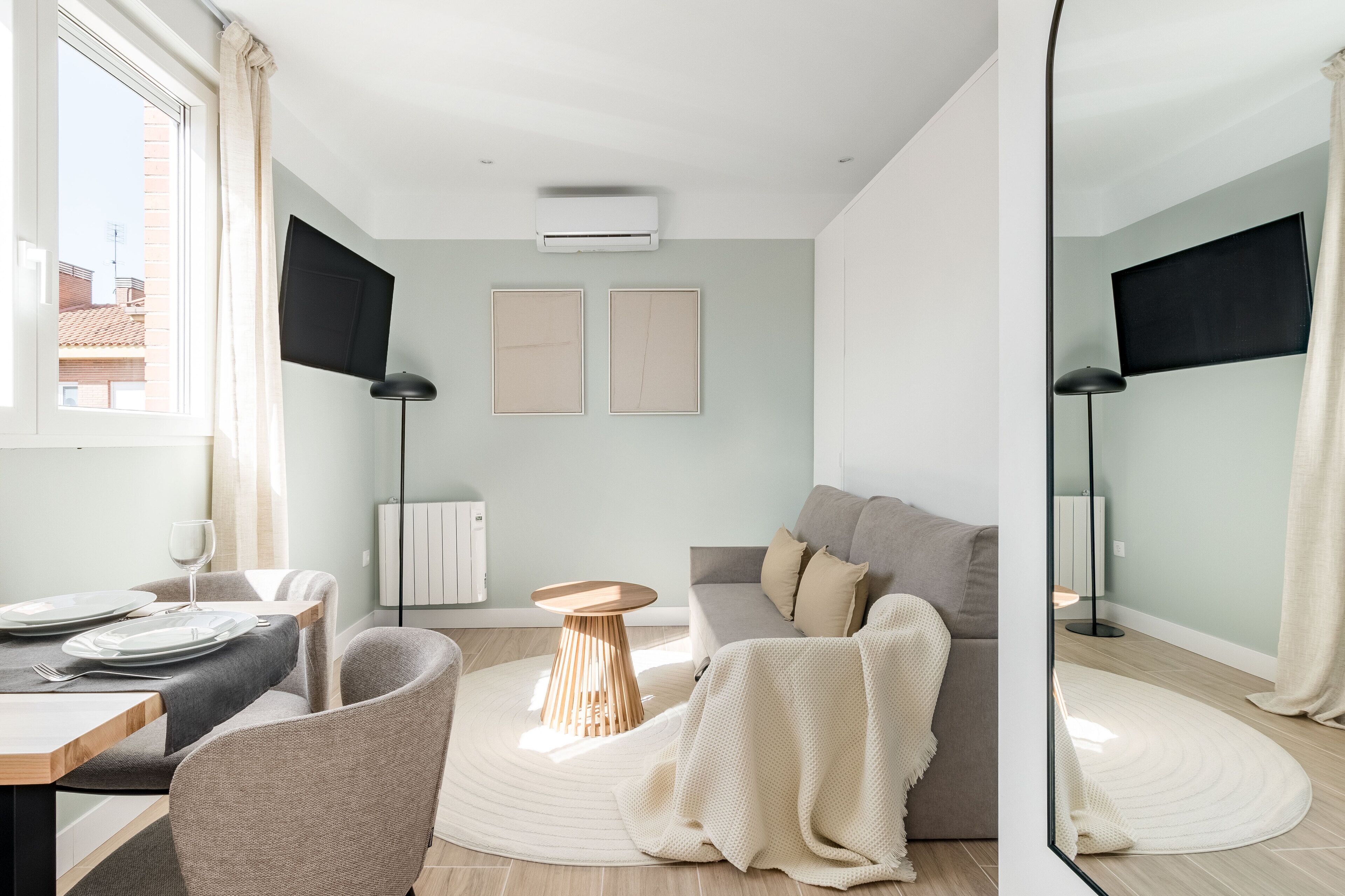 Un salon moderne comprenant un coin repas, un canapé gris, une table basse ronde en bois et deux tableaux encadrés accrochés au mur.