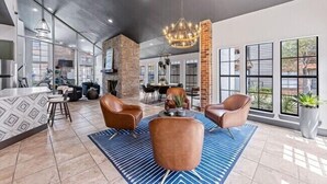 A spacious lobby with a high ceiling, a chandelier, leather chairs, a patterned rug, and large windows offering views of the outdoors.