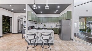 A modern kitchen with a central island, green cabinets, and a large window.