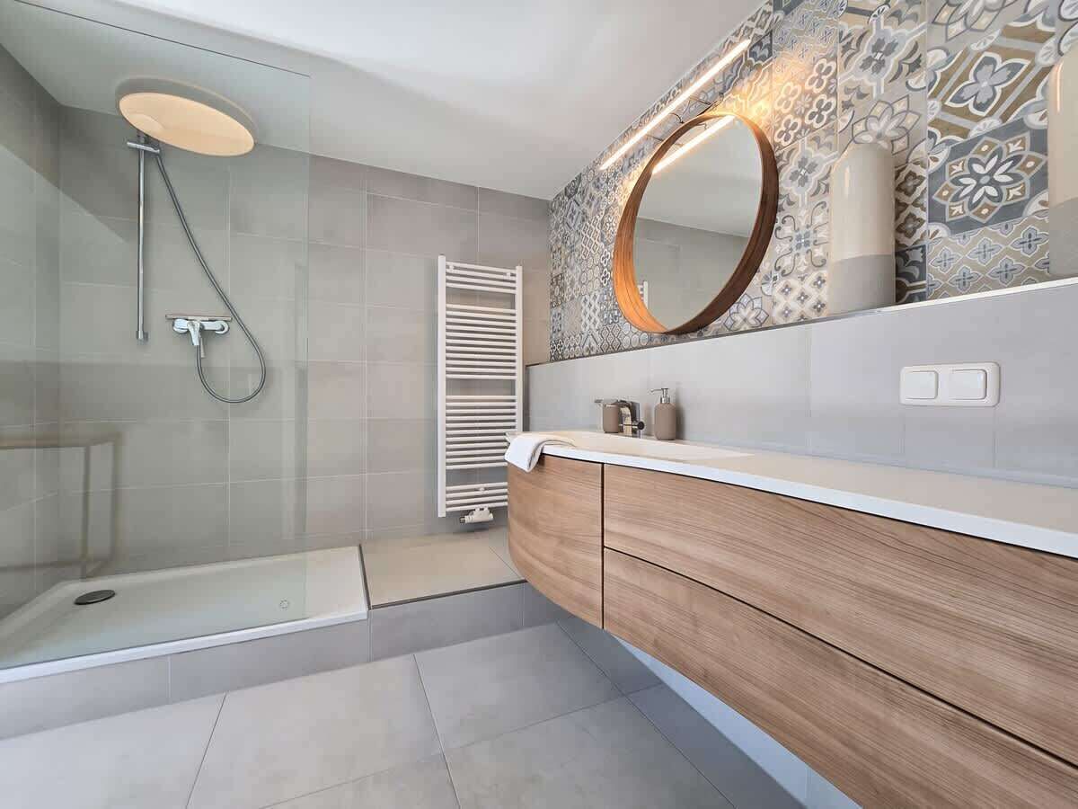 Ein modernes Badezimmer mit einer gläsernen Dusche, einem Holzbadezimmer-Möbelstück und einer Wandfliesen-Verkleidung.