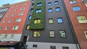 A multi-story building with a modern facade, featuring a vertical garden on one side and a mix of brick and smooth surfaces on the other. - Alpha Apartments: Green Design Studio for 2P (Dortmund)