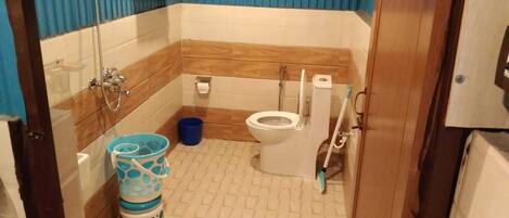 A small bathroom with a toilet, a shower, and a sink. There is a blue bucket and a white trash bin.
