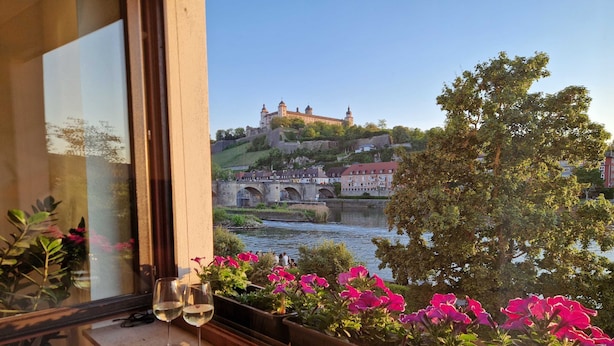 Vista desde una ventana, con una mesa mostrando dos copas de vino y un arreglo floral.