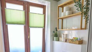 A bathroom with a bathtub, toilet, and window with blinds.