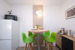 A compact kitchen with a microwave, toaster, and coffee maker. There are two green chairs around a small wooden table. - Alte Mainbrücke Apartment | Panoramic View (Würzburg)