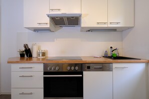 A kitchen with white cabinets, a stainless steel oven, a dishwasher, and a wooden countertop. - Alte Mainbrücke Apartment | Panoramic View (Würzburg)