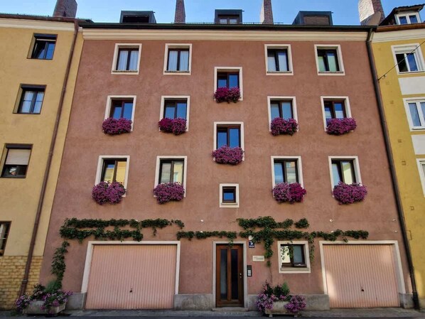 Un edificio de varios pisos con una hilera de ventanas en la planta baja, algunas con macetas de flores.