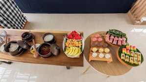 Une table à manger avec divers plats et accompagnements, notamment des bols de riz, une assiette de fruits coupés et un plateau de desserts colorés.