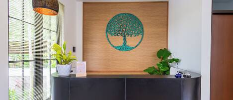 A reception desk with a wooden backdrop, a potted plant, and a hanging light fixture.