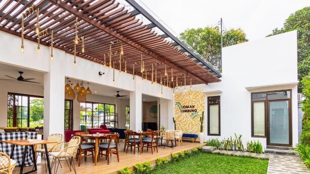 Un espace extérieur moderne, aménagé avec des tables et des chaises en bois, une pergola agrémentée de guirlandes lumineuses et une pelouse bien entretenue.