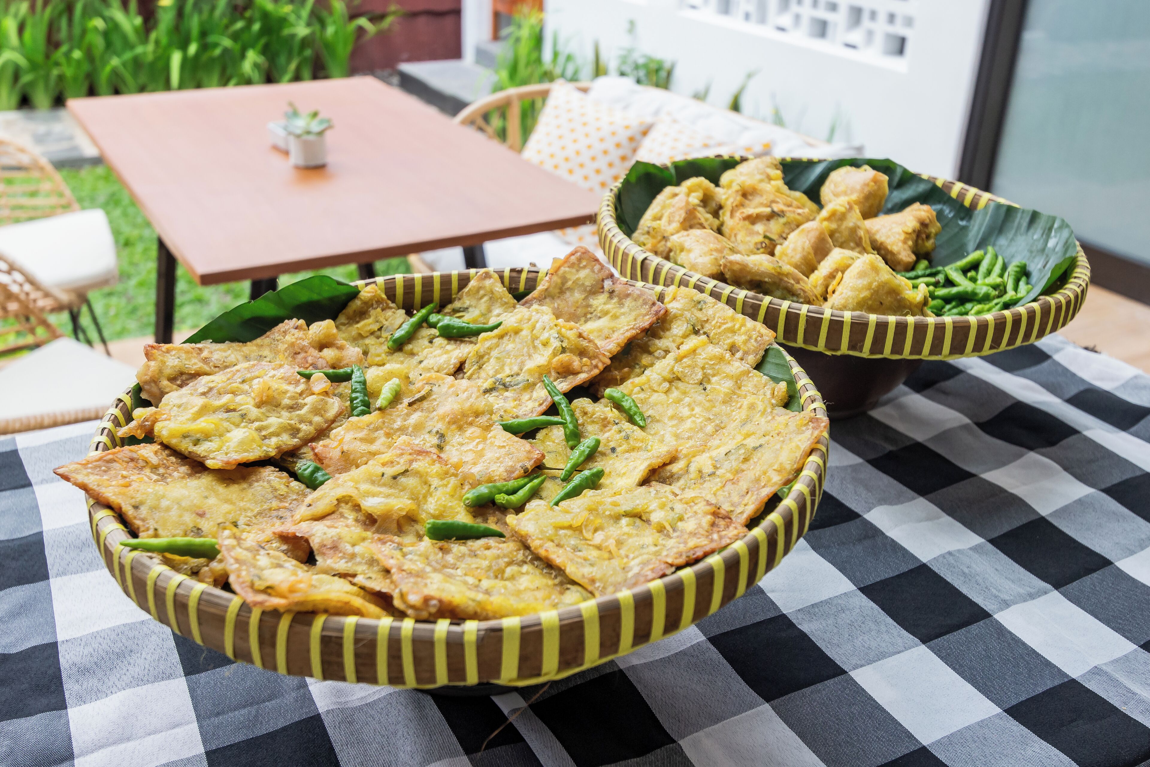 A checkered tablecloth with two woven baskets containing fried food items.