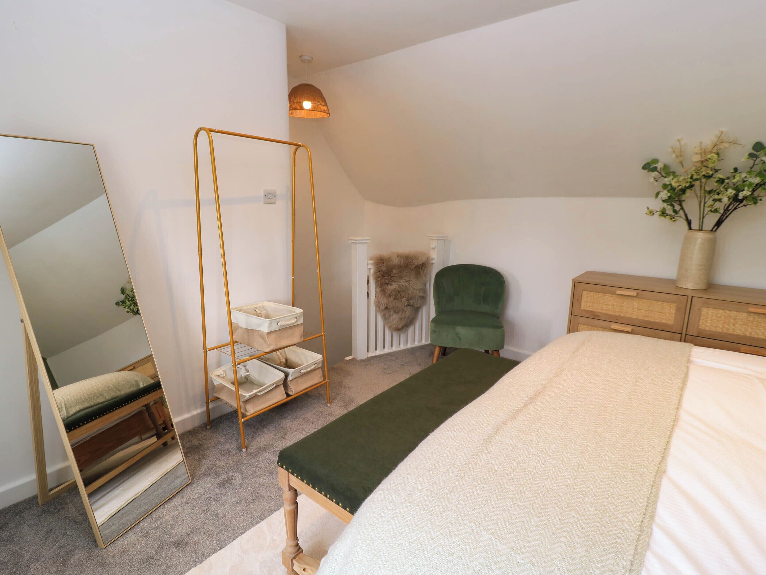 A bedroom with a large bed, a green armchair, a wooden dresser, a mirror, a hanging light fixture, and a radiator.