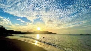 A beach scene with a clear sky, calm sea, and distant mountains.