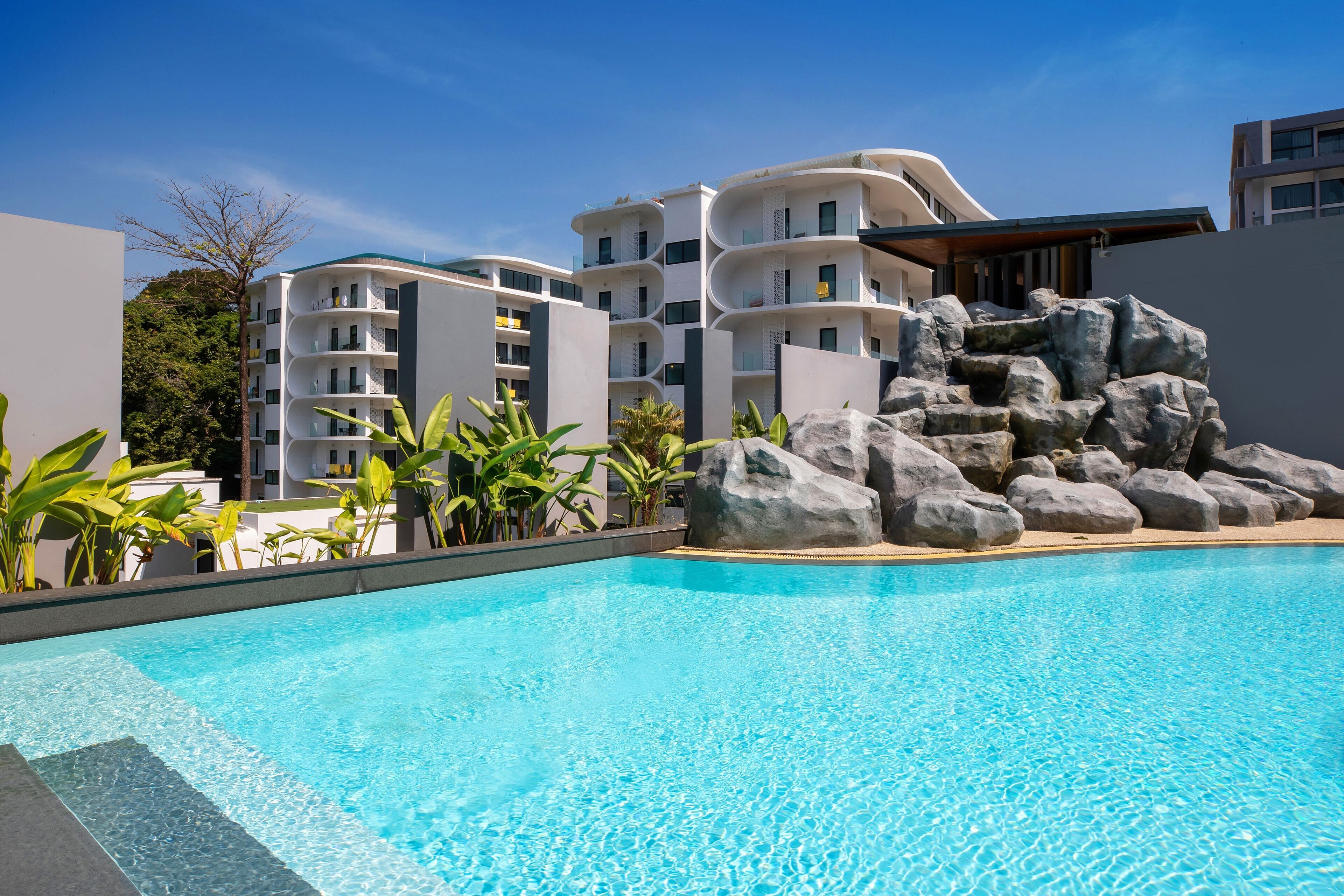 Una piscina con agua azul cristalina, rodeada de edificios blancos y una formación rocosa.
