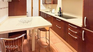 A compact kitchen with a countertop, a sink, and a stove. There are stools and cabinets with drawers. - XILGAR Maracaibo Apartment Central next to the Beach (Sanxenxo)