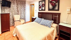 A hotel room with a bed, a chair, a TV, and artwork on the wall. - XILGAR Maracaibo Apartment Central next to the Beach (Sanxenxo)