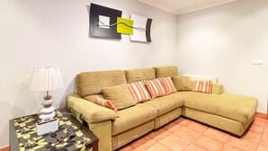 A living room with a beige sofa, striped pillows, a small table with a lamp, and a wall with abstract art. - XILGAR Maracaibo Apartment Central next to the Beach (Sanxenxo)