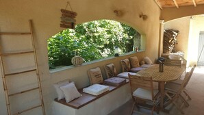 A cozy outdoor seating area with a wooden table and chairs, a cushioned bench, and a window overlooking lush greenery. - Vacation rental house with pool ALTHEN LES PALUDS  LS6-71 (Althen des Paluds)