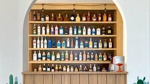 A wooden bar with shelves of various liquor bottles, two potted cacti, and a coffee machine. - Sunset Paradise Canggu (Canggu)
