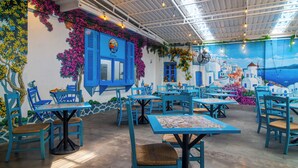 A restaurant with blue tables and chairs, a mural of a coastal town, and a clock on the wall. - Sunset Paradise Canggu (Canggu)
